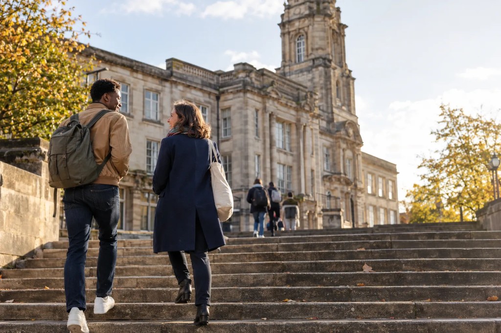Two students walking toward a UK university building at the start of a four year degree.